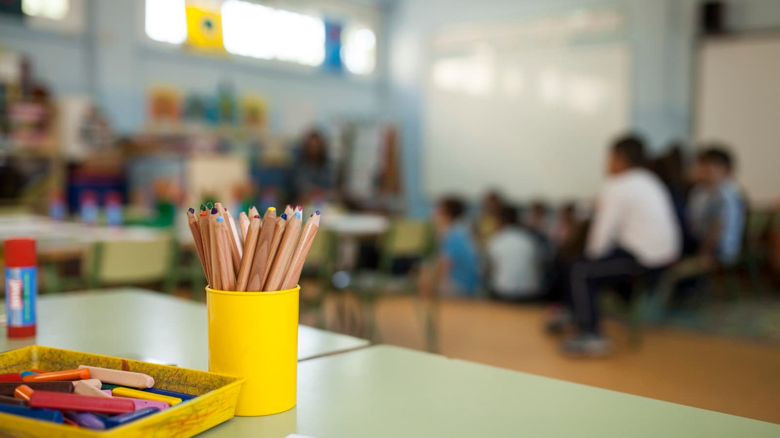 Kubek z kredkami i pojemnik z kredkami na ławce, w tle rozmyta klasa
