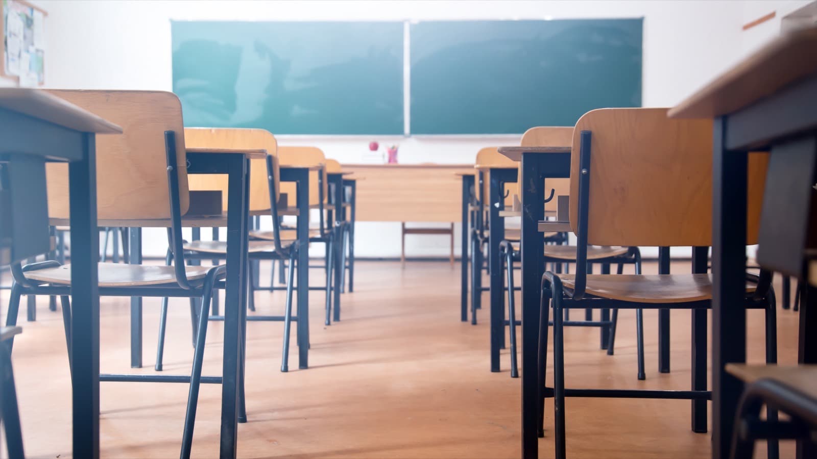 Pusta sala lekcyjna z rzędami ławek i krzeseł, w głębi zielona tablica