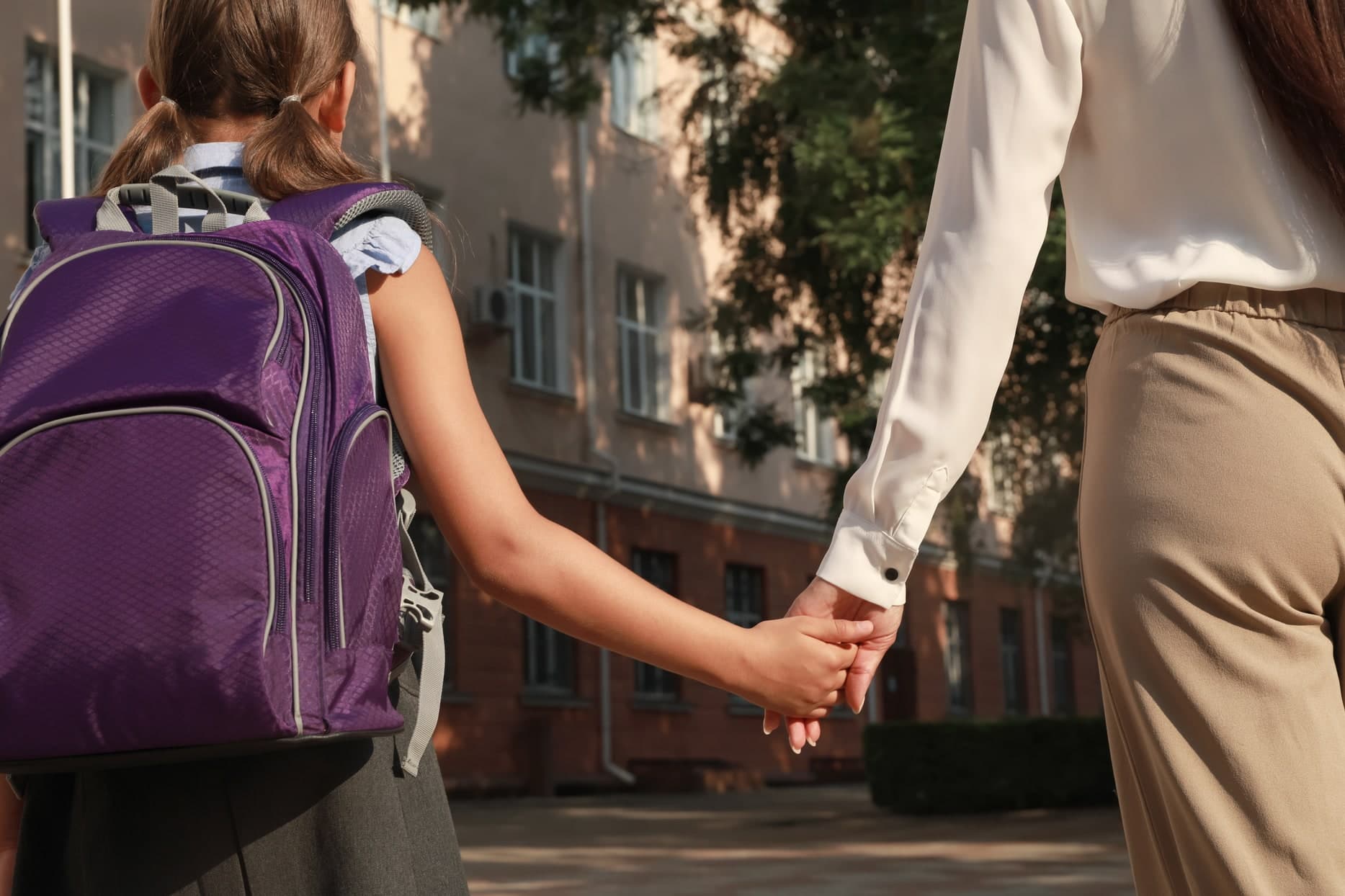 Dziecko z plecakiem stoi przed drzwiami szkoły — gotowość szkolna