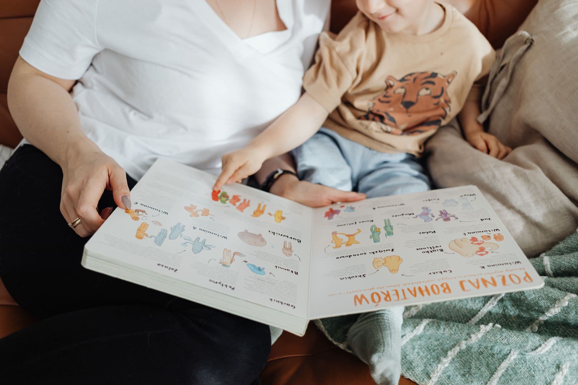 Mama i kilkuletni chłopiec czytają razem ilustrowaną książkę na kanapie. Fot. Kaboompics / Pexels